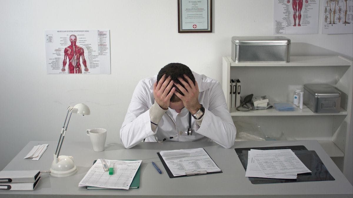 tired doctor holding head: © fancystudio - stock.adobe.com